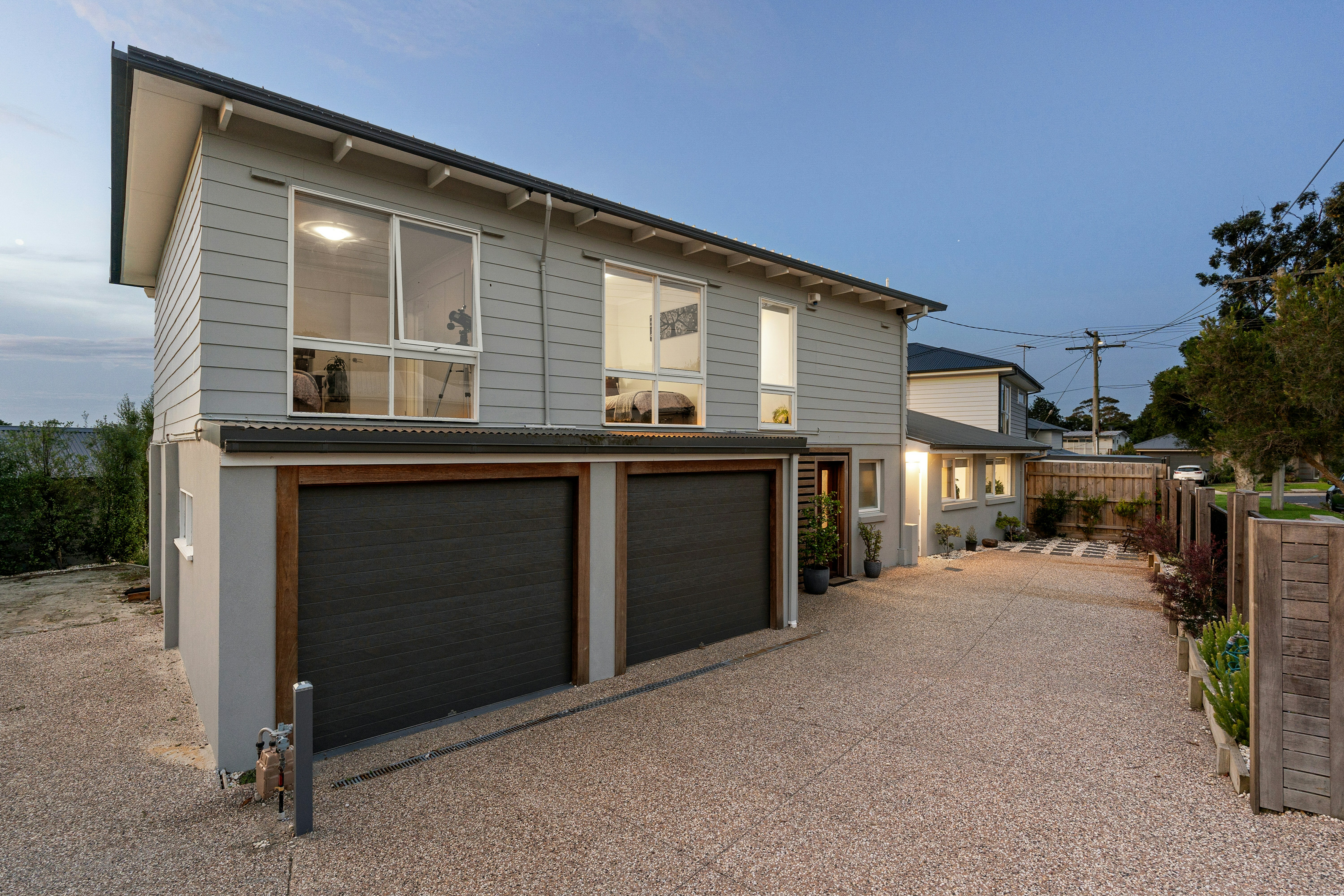 A modern home has grey siding, black garage doors and white trimmed windows for a clean look.