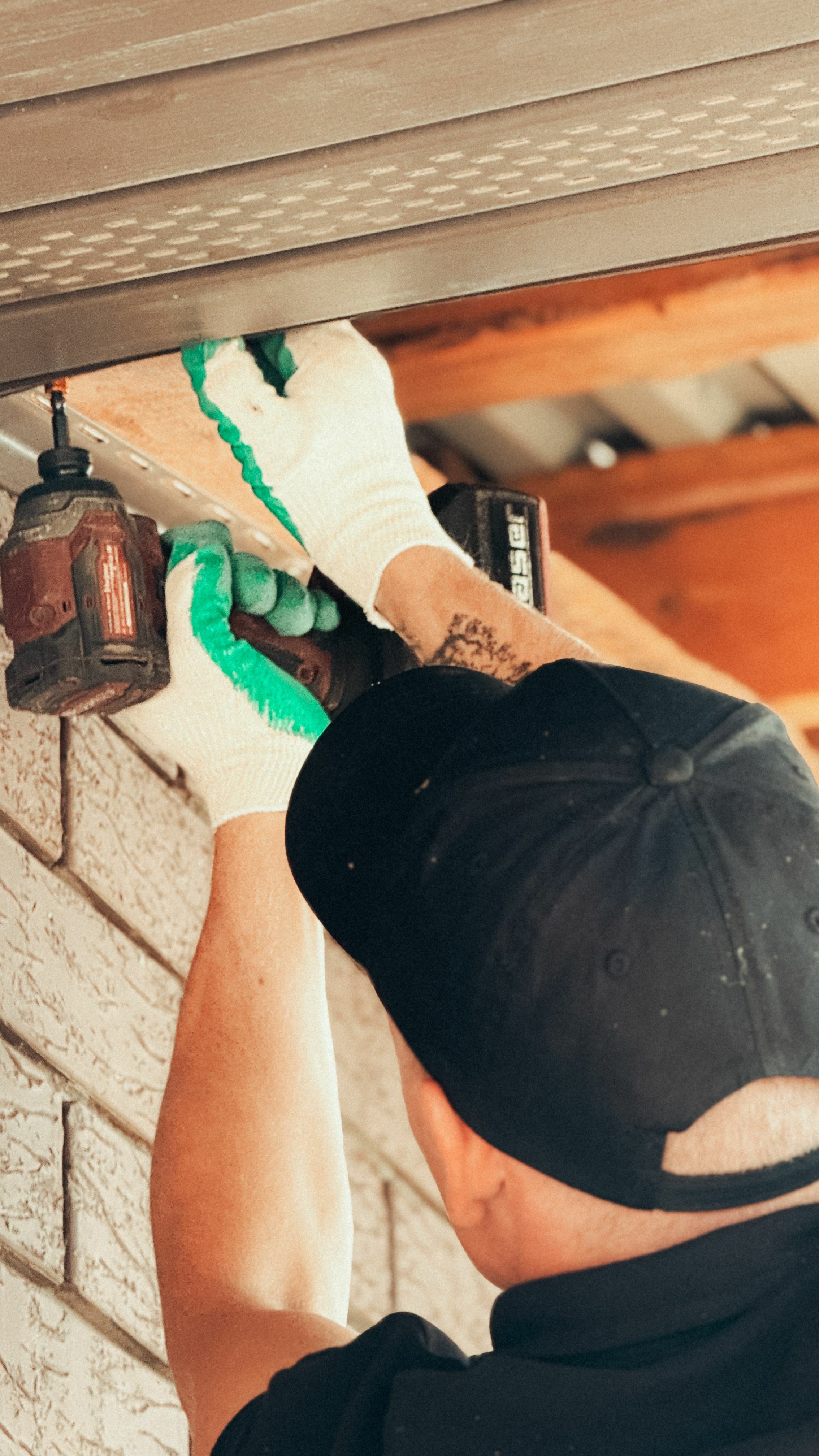 A man in a black cap and green and white gloves installs vented soffits into the underside of a home’s roof.