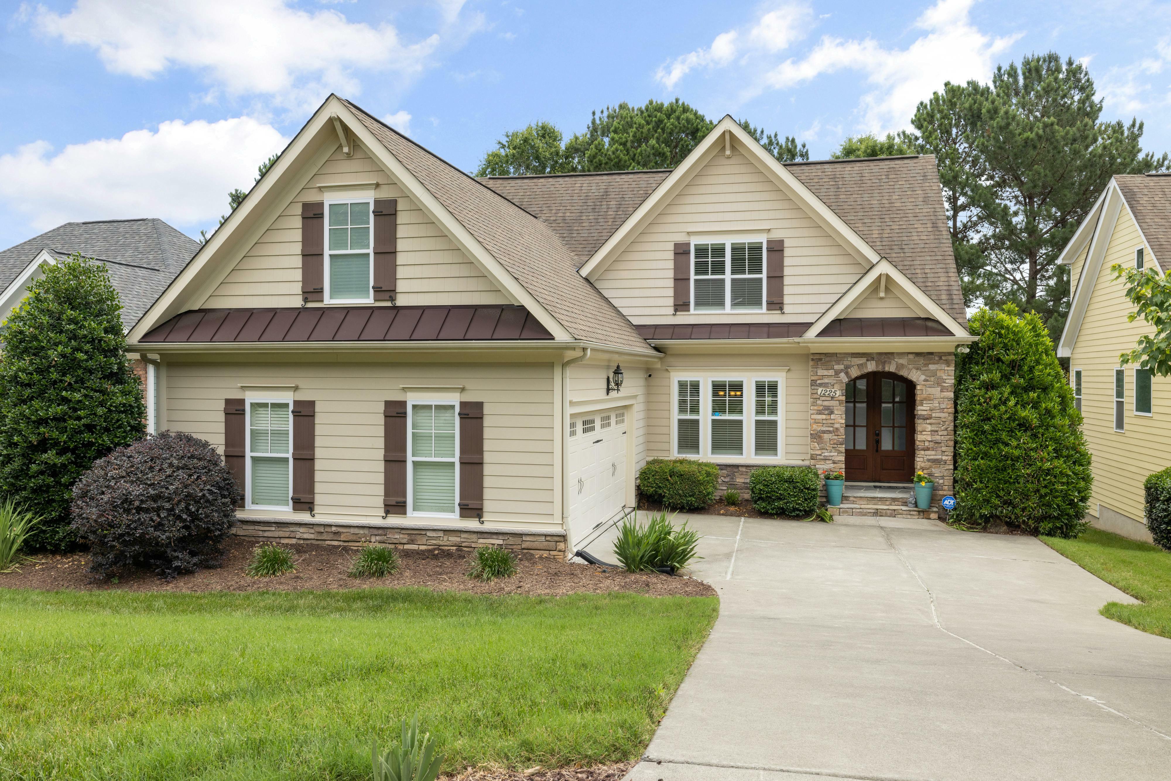 A two-story house with tan siding has brown shutters and a paved driveway.