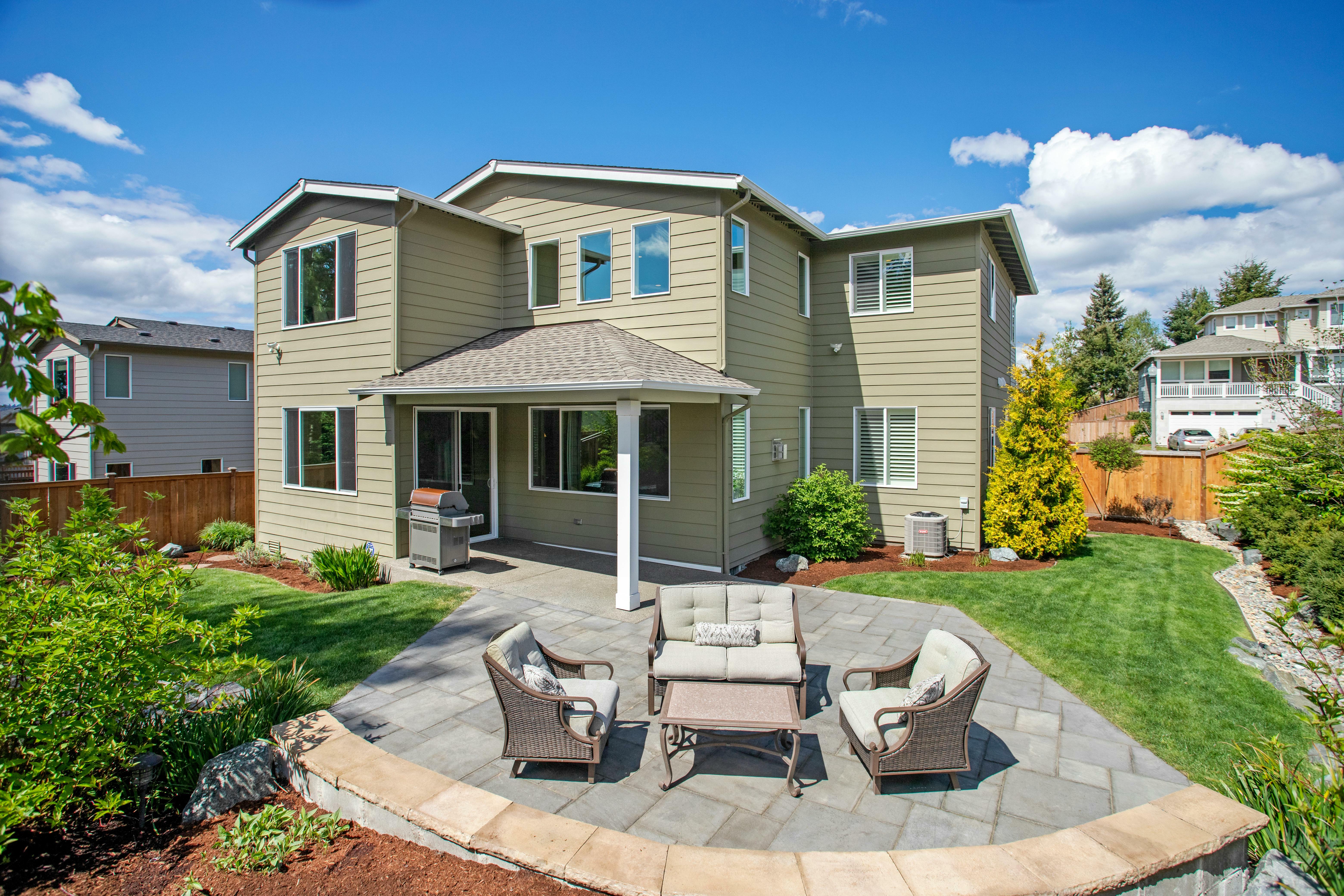A backyard has various landscaping zones and a large paved patio for outdoor lounging