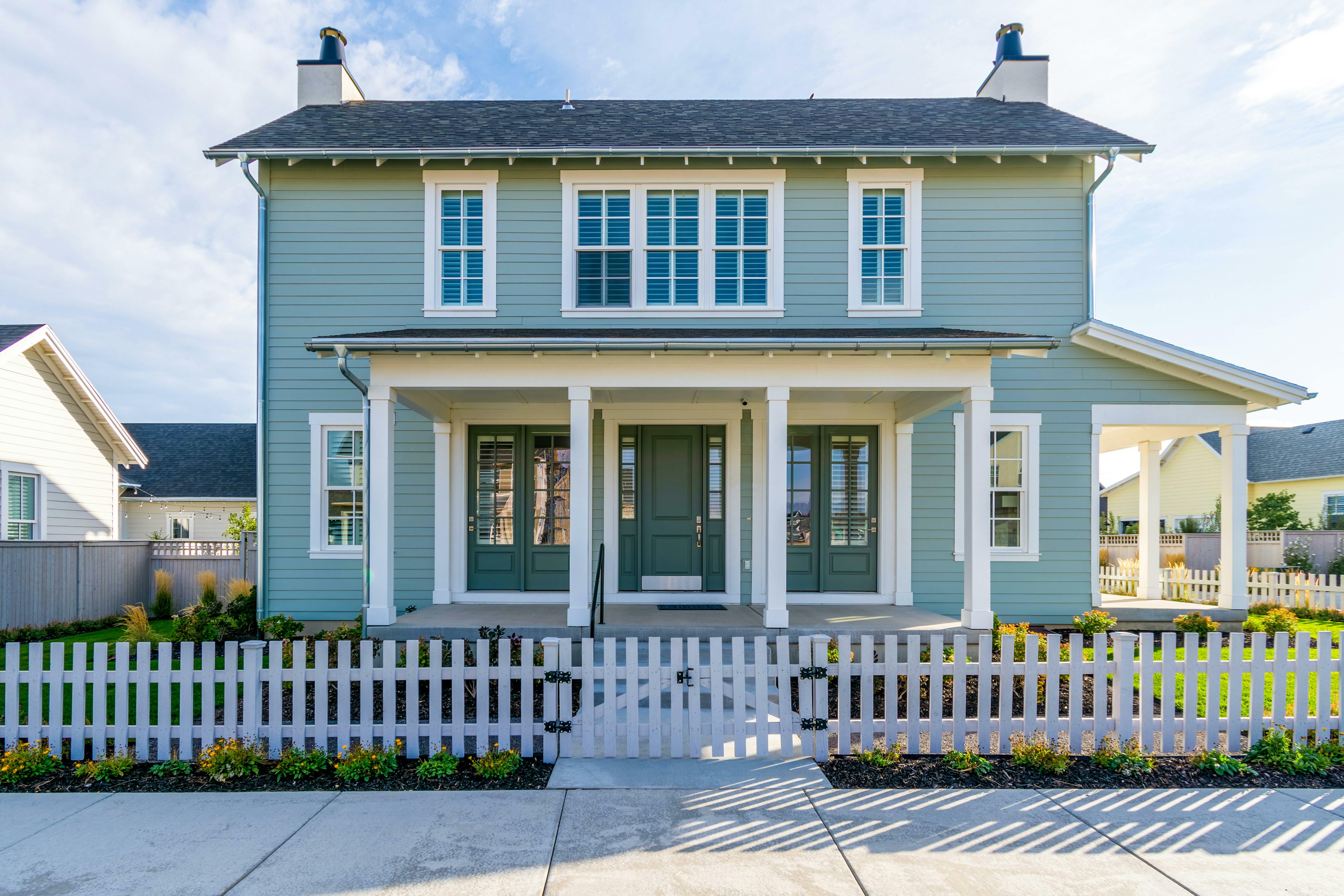 A modern home features blue siding, stunning windows, green doors and white trim.