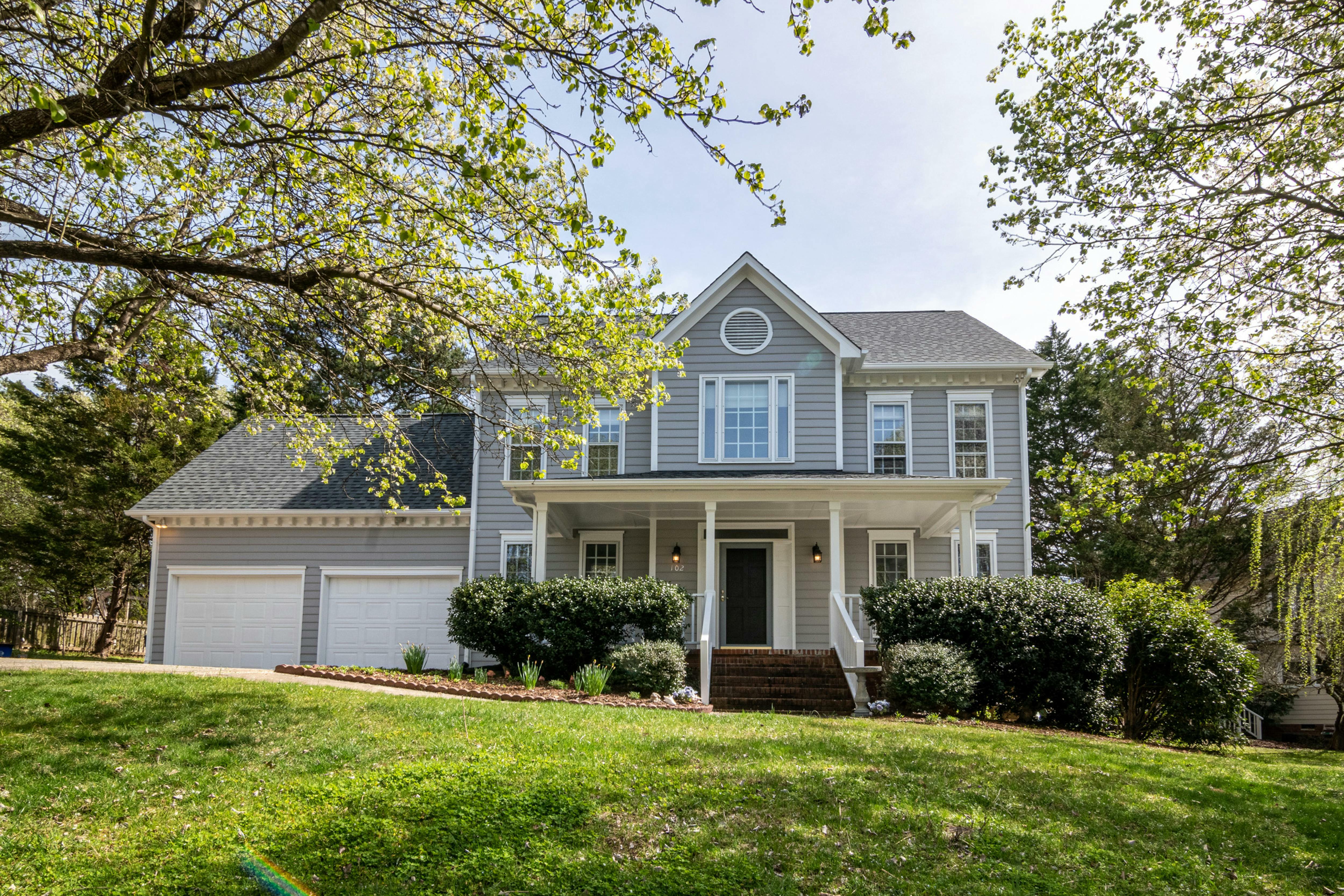 A two-story house with grey siding has white trim and a paved driveway.