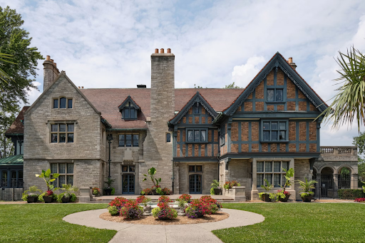 Exterior of a large Tudor-style home with a manicured front lawn and landscaped garden.