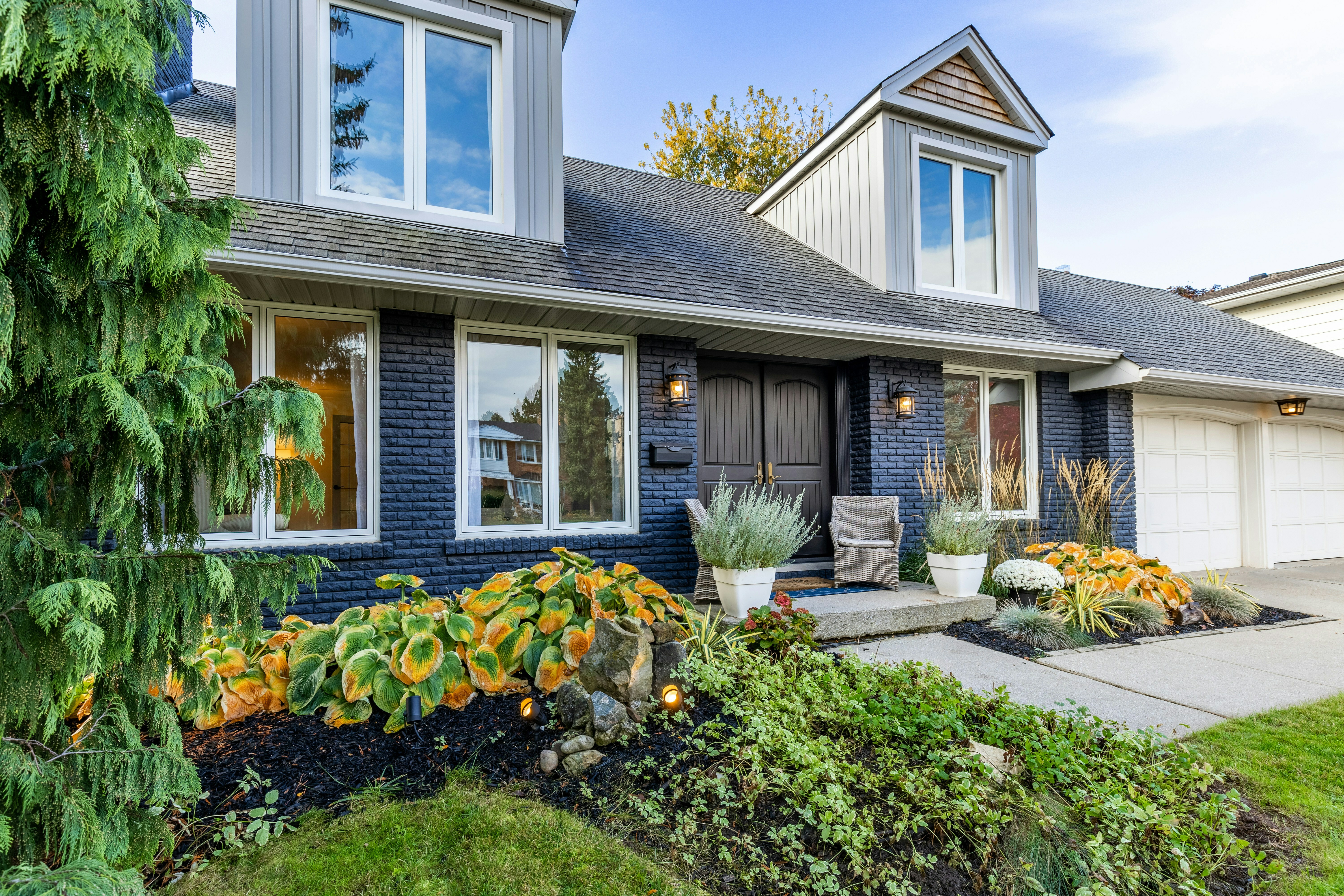 A blue home has white trim, black doors and a paved driveway leading to a two-car garage.