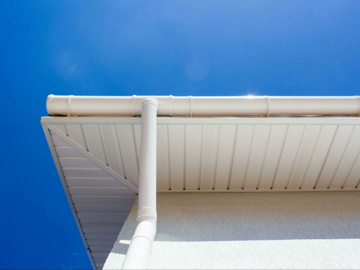A close-up of white soffit vents on a home, with a white downspout leading down the exterior wall.